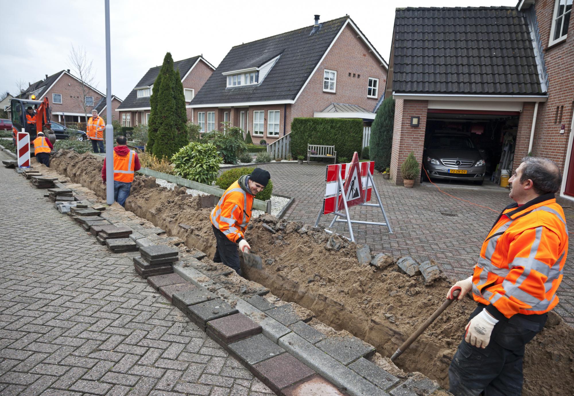 Workmen bring up pavement to lay fibre optic cables.