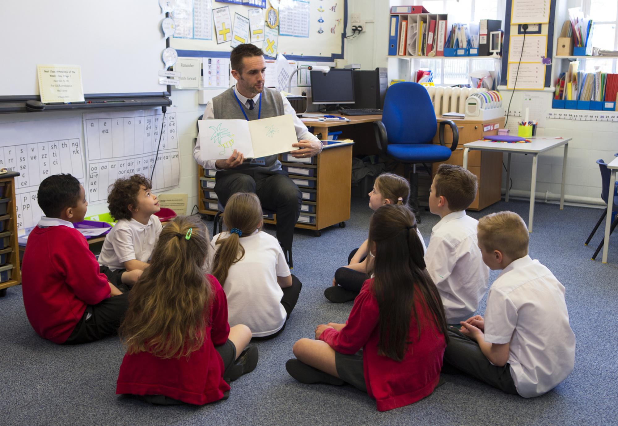 Children sit with teacher as he reads a story.
