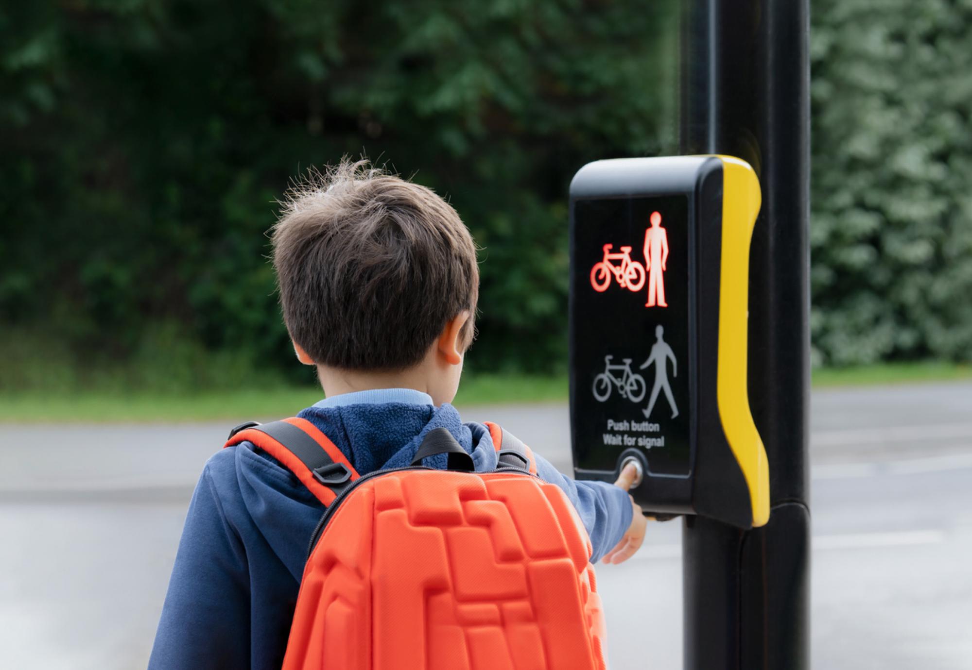 School kid pressing a button at traffic lights on pedestrian crossing on way to school