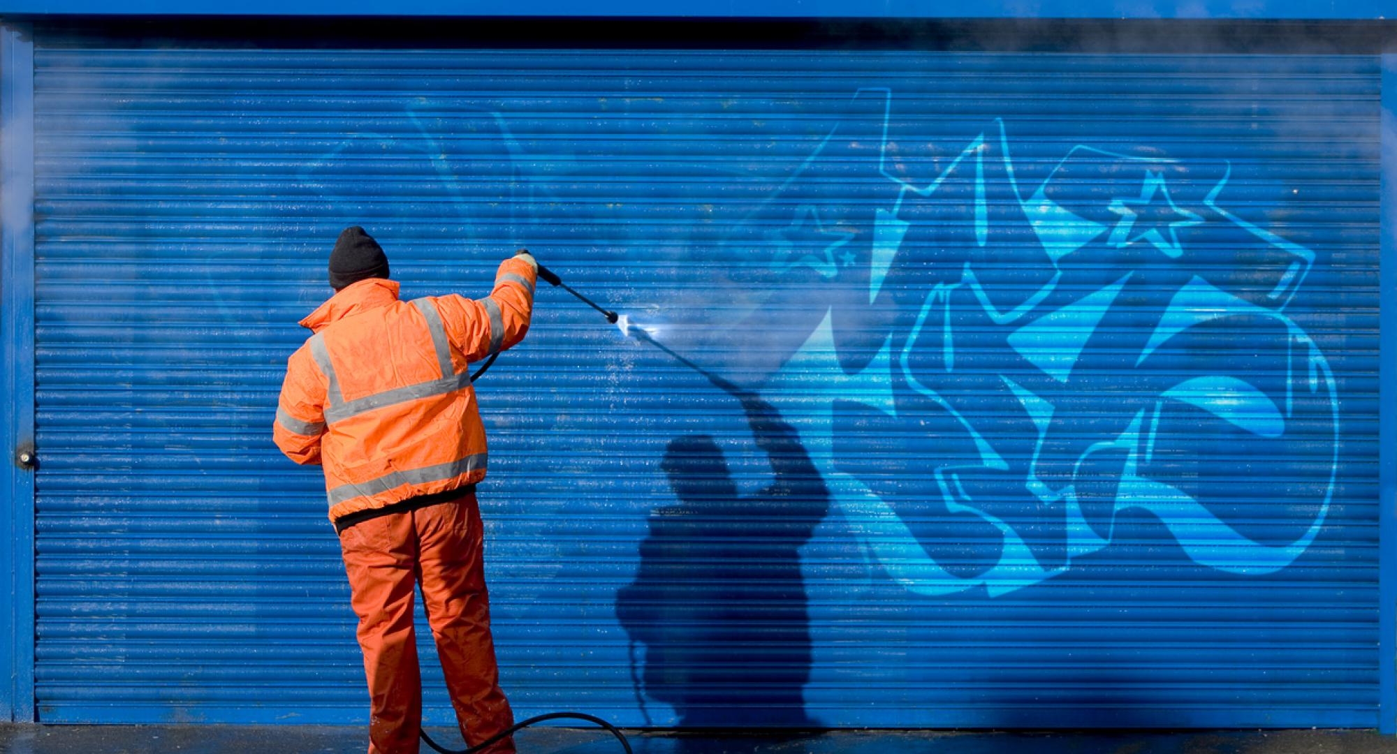 Man removes graffiti from shop front.