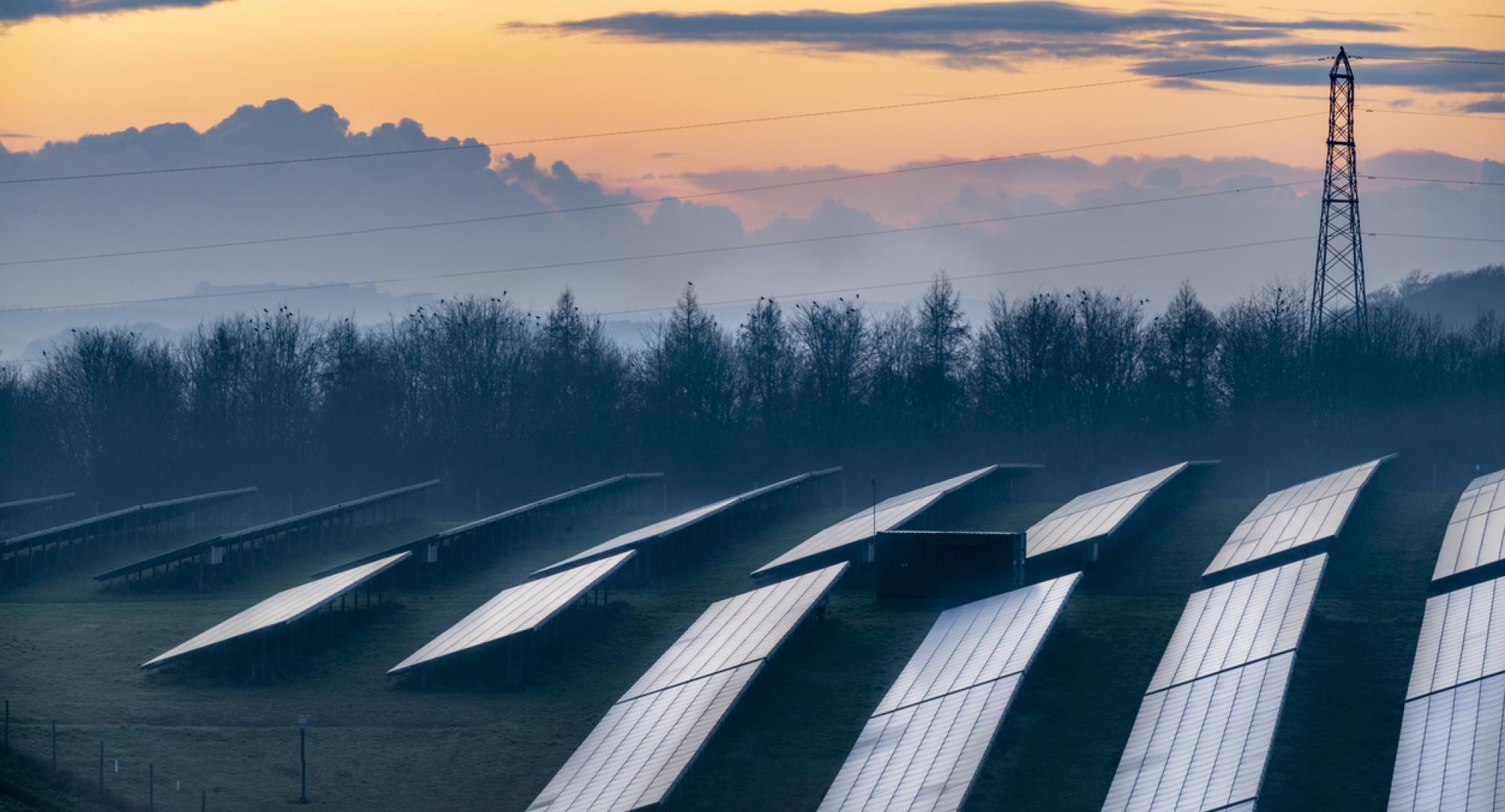 Solar energy park and conventional electricity pylon at sunset, Hampshire, England