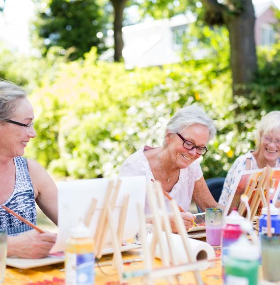 Group of happy elderly women attending an outdoor art class in a garden.