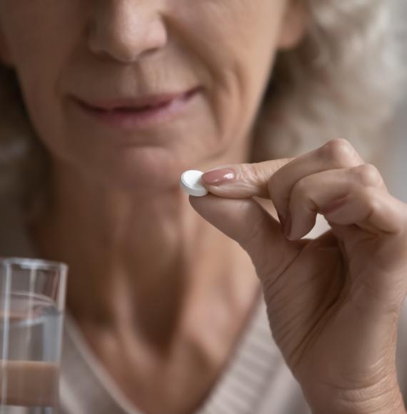 Elderly woman holds pill in her hand ready to be taken.