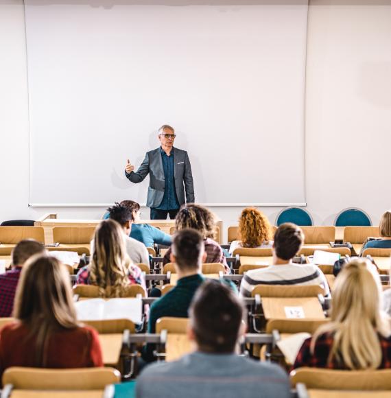 Lecturer stands teaching students in a lecture hall.