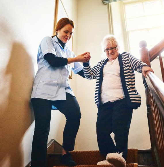 Social care worker helping woman walk down stairs