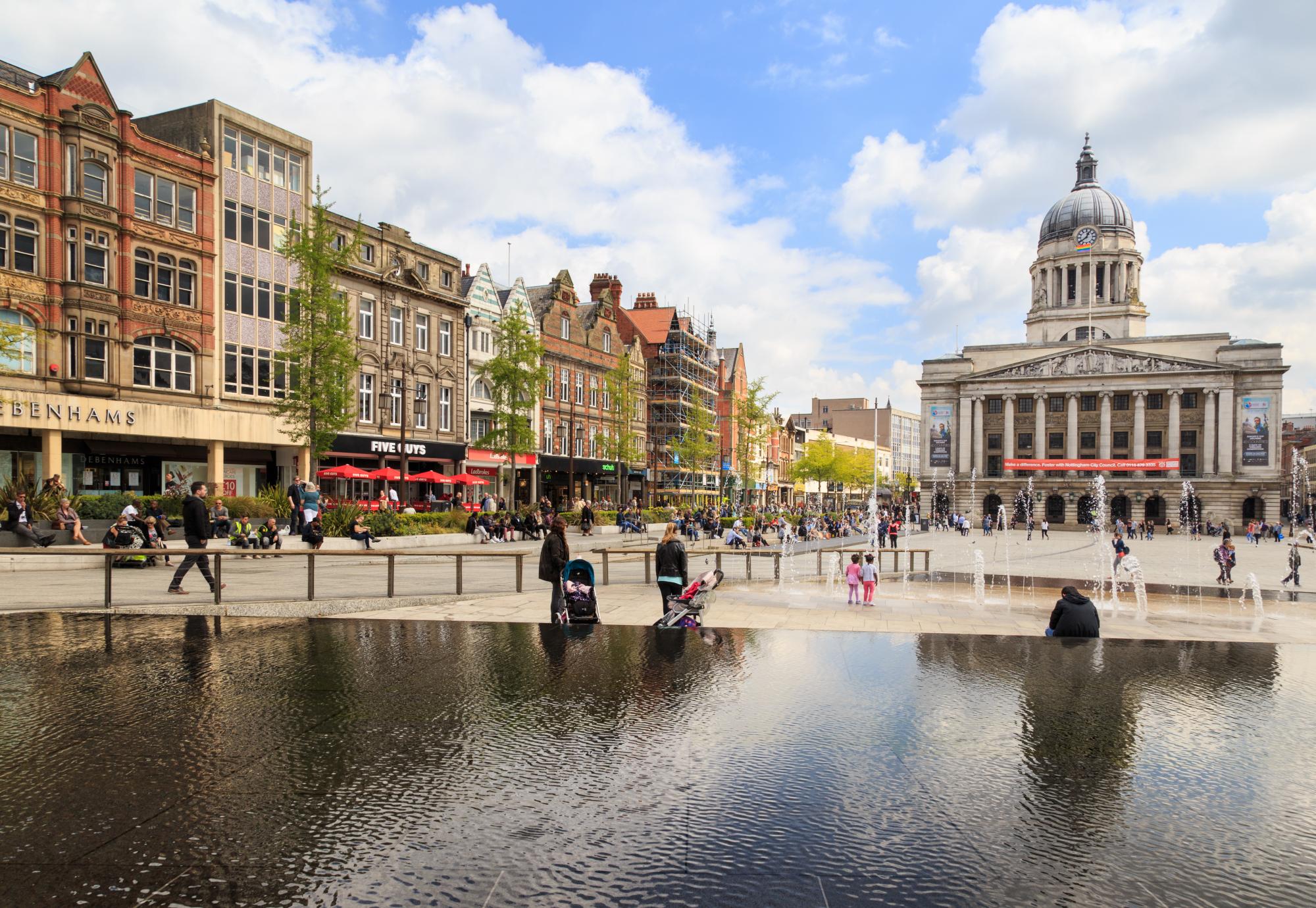 Various people sitting, walking, visiting in the main Market Square, Nottingham Council House building behind.