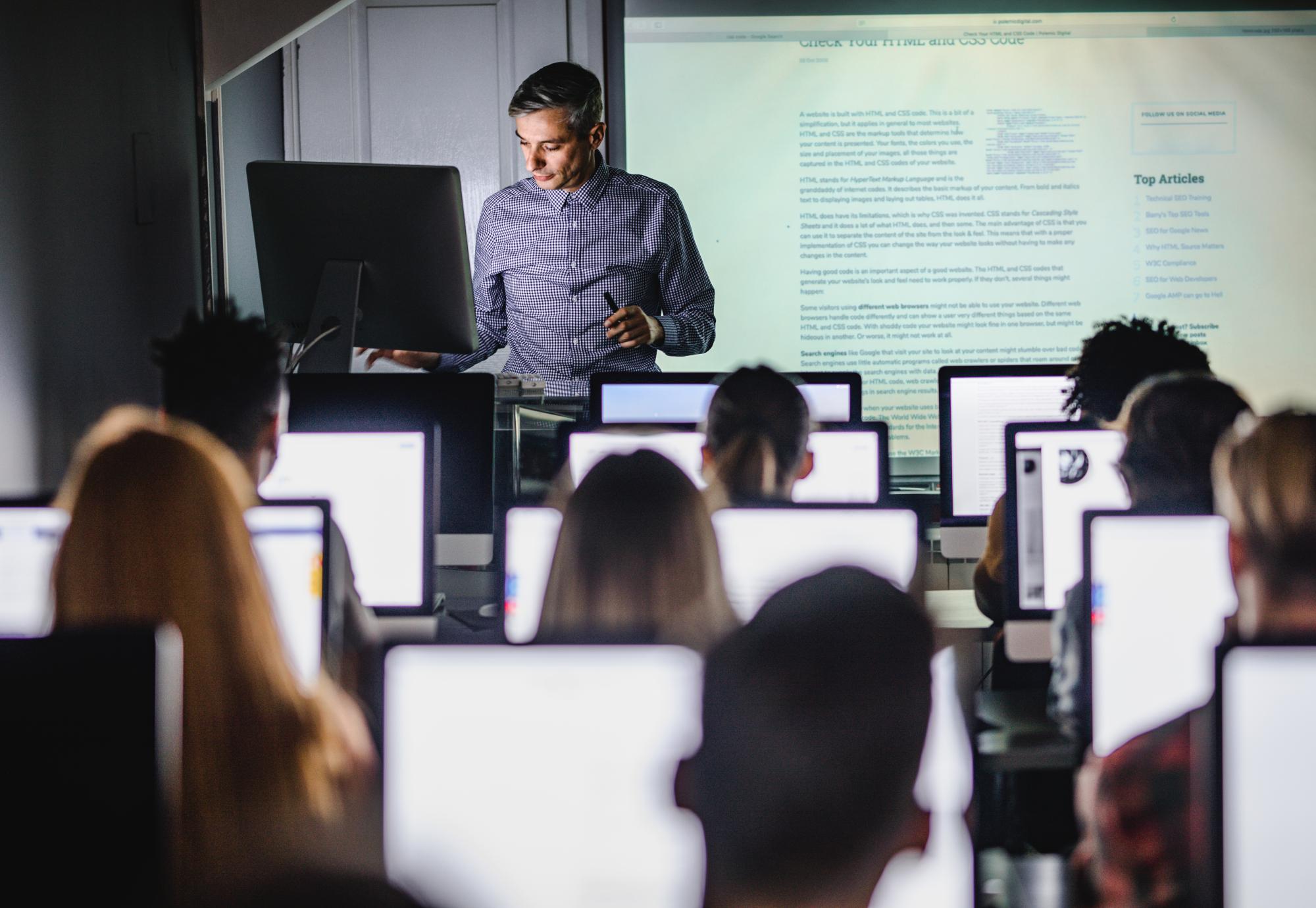 Male teacher giving a lecture from desktop PC during a class at computer lab.