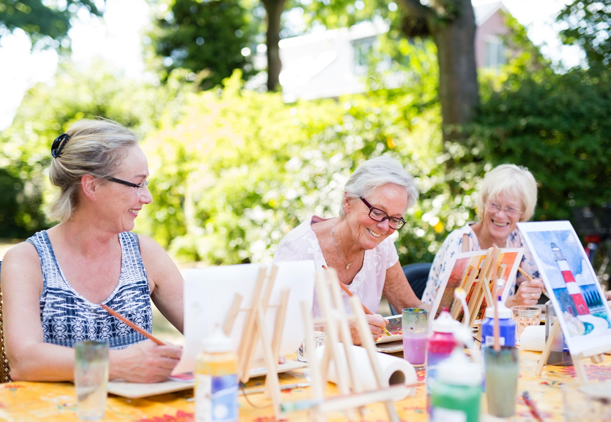 Group of happy elderly women attending an outdoor art class in a garden.
