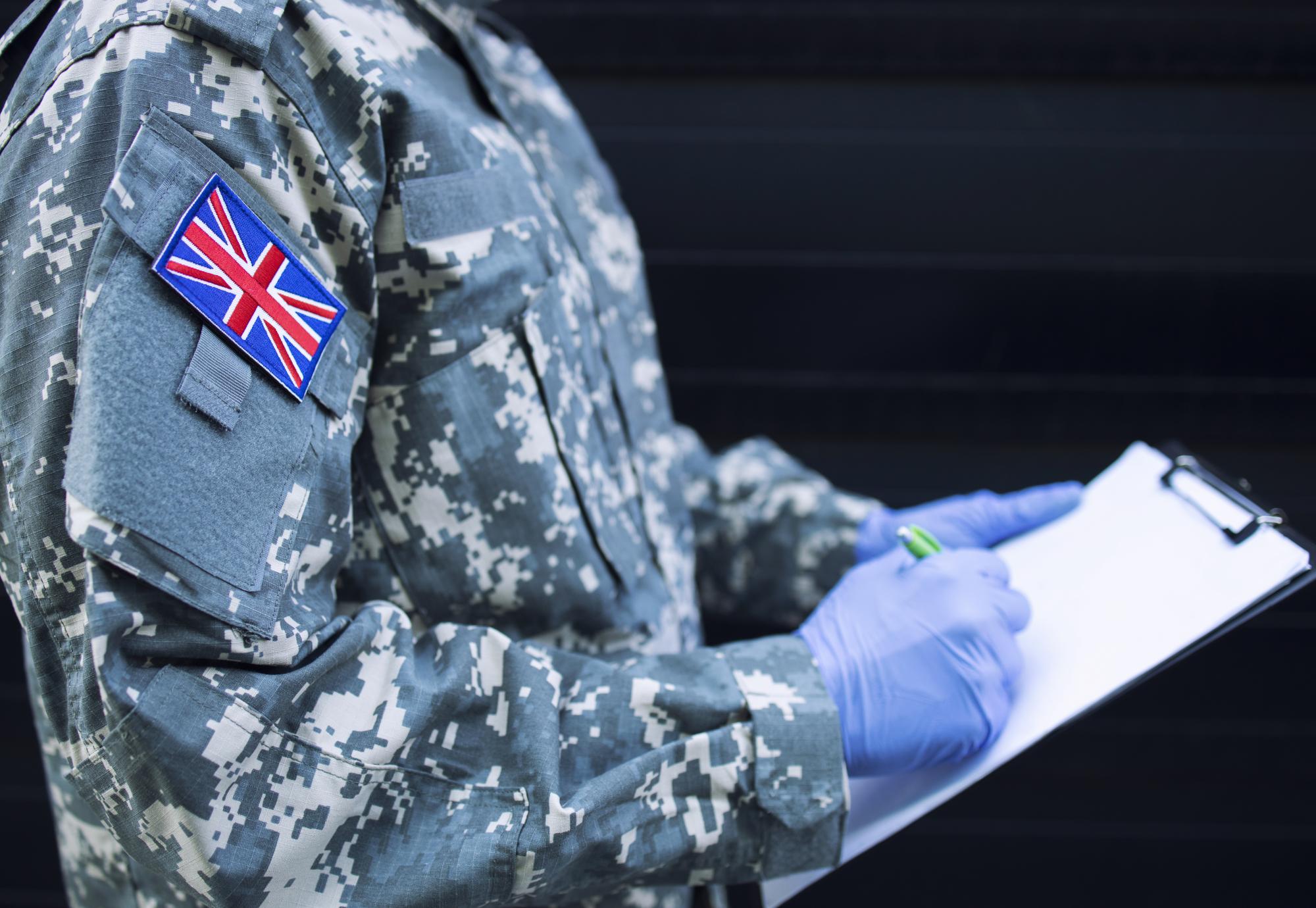 Britain soldier in camouflage uniform with rubber gloves, mask guarding in front of hospital's door controlling who gets in or out.