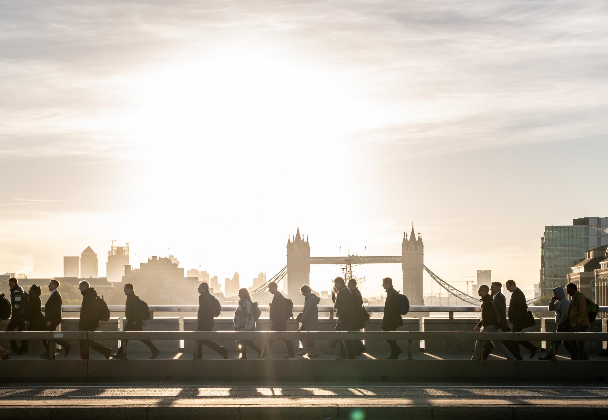 Morning rush hour across London Bridge at dawn. Bright sunlight and Tower Bridge in the background