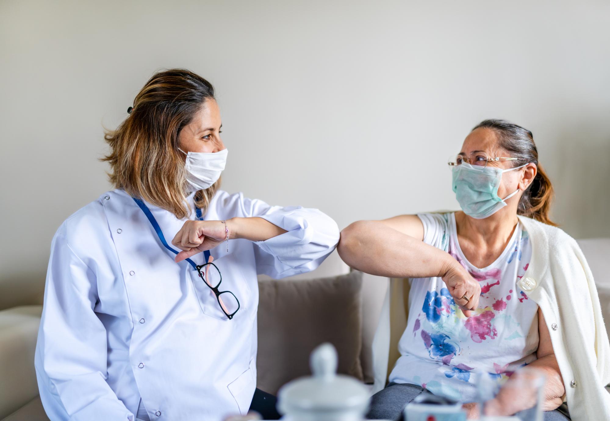 Nurse and patient bumping elbows in a care home, with face coverings on.