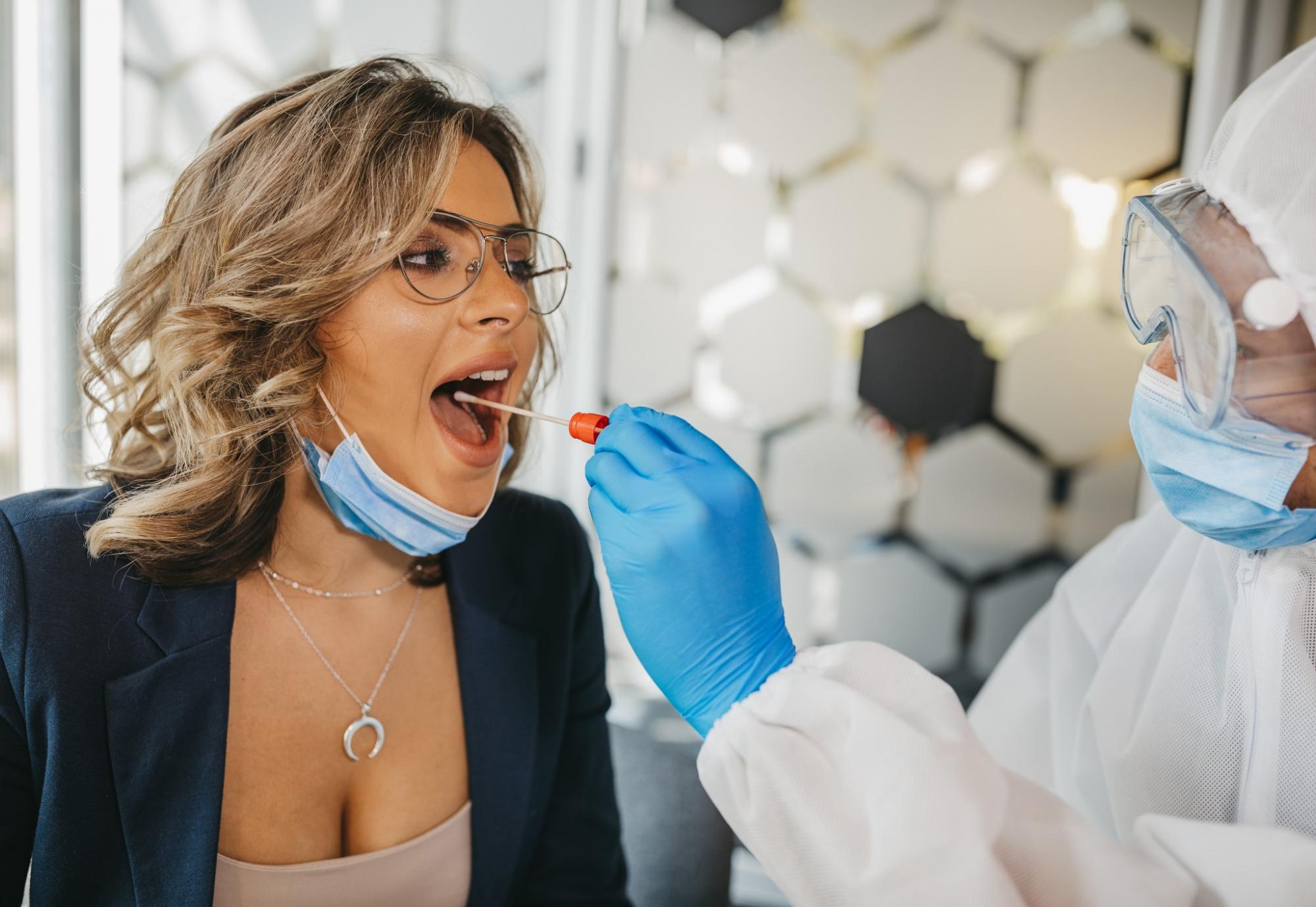 Woman in glasses receives Covid test from man wearing PPE.