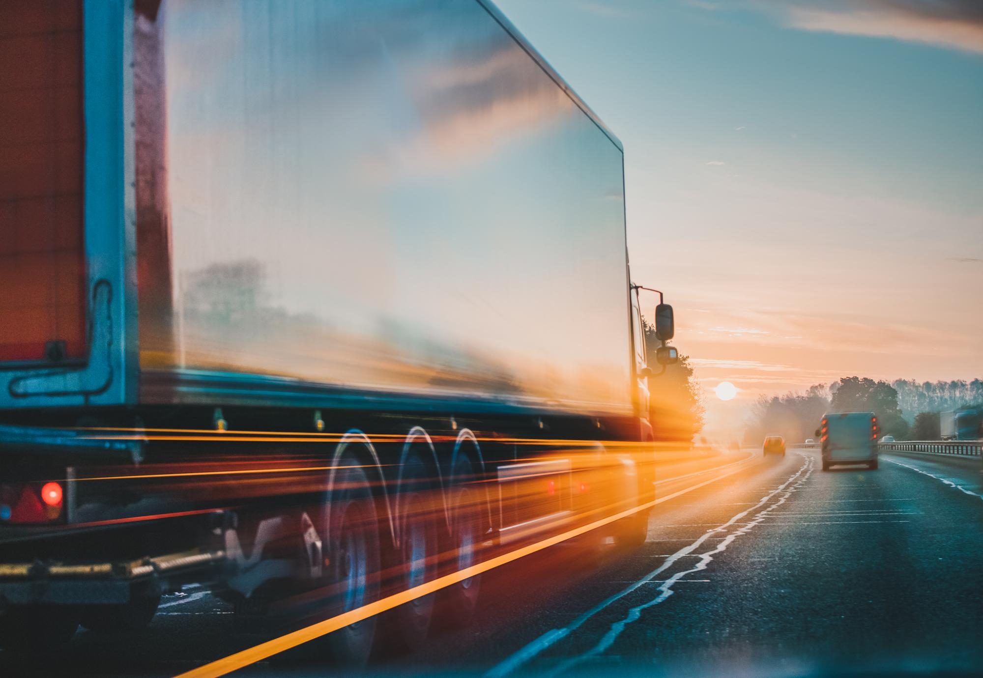 HGV travelling down an A-road, with the sun setting up ahead.