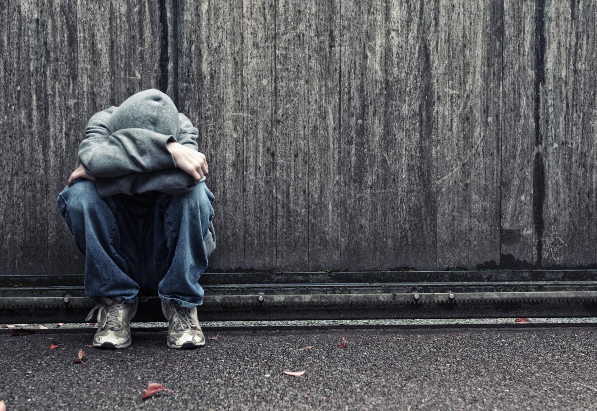 Homeless youth sits on the street looking sad. 