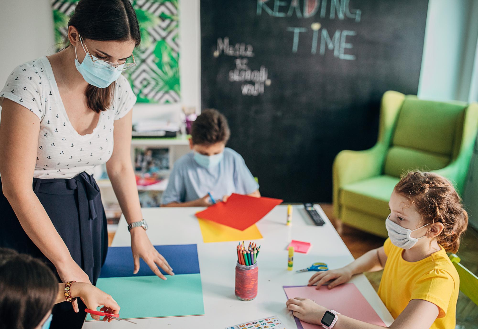 Teacher in a face mask teaches small child.