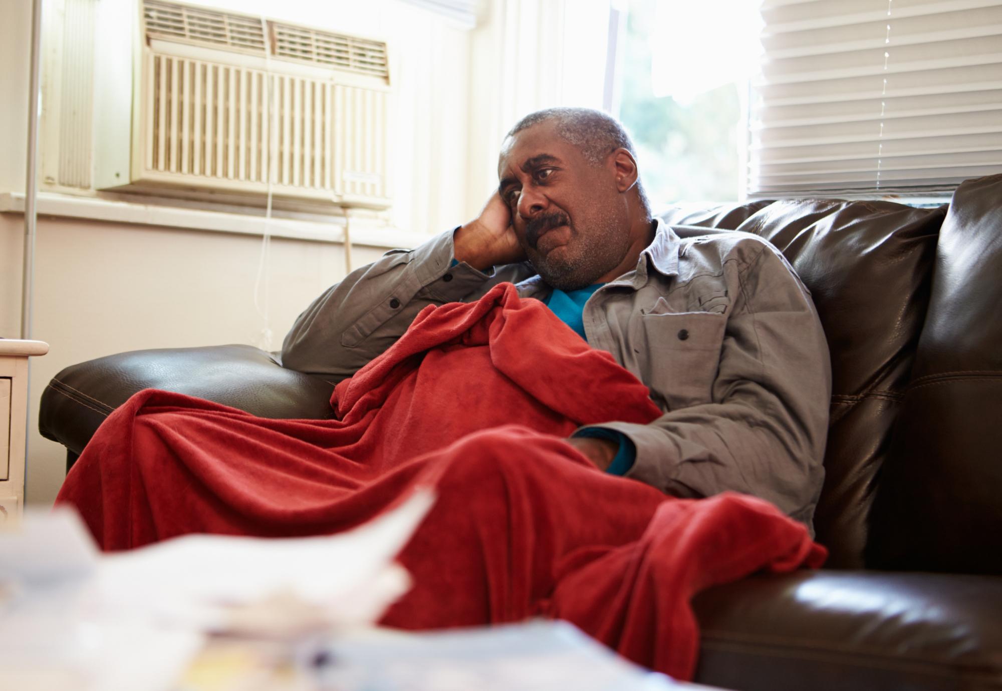 Man is cold in house with blanket around him.