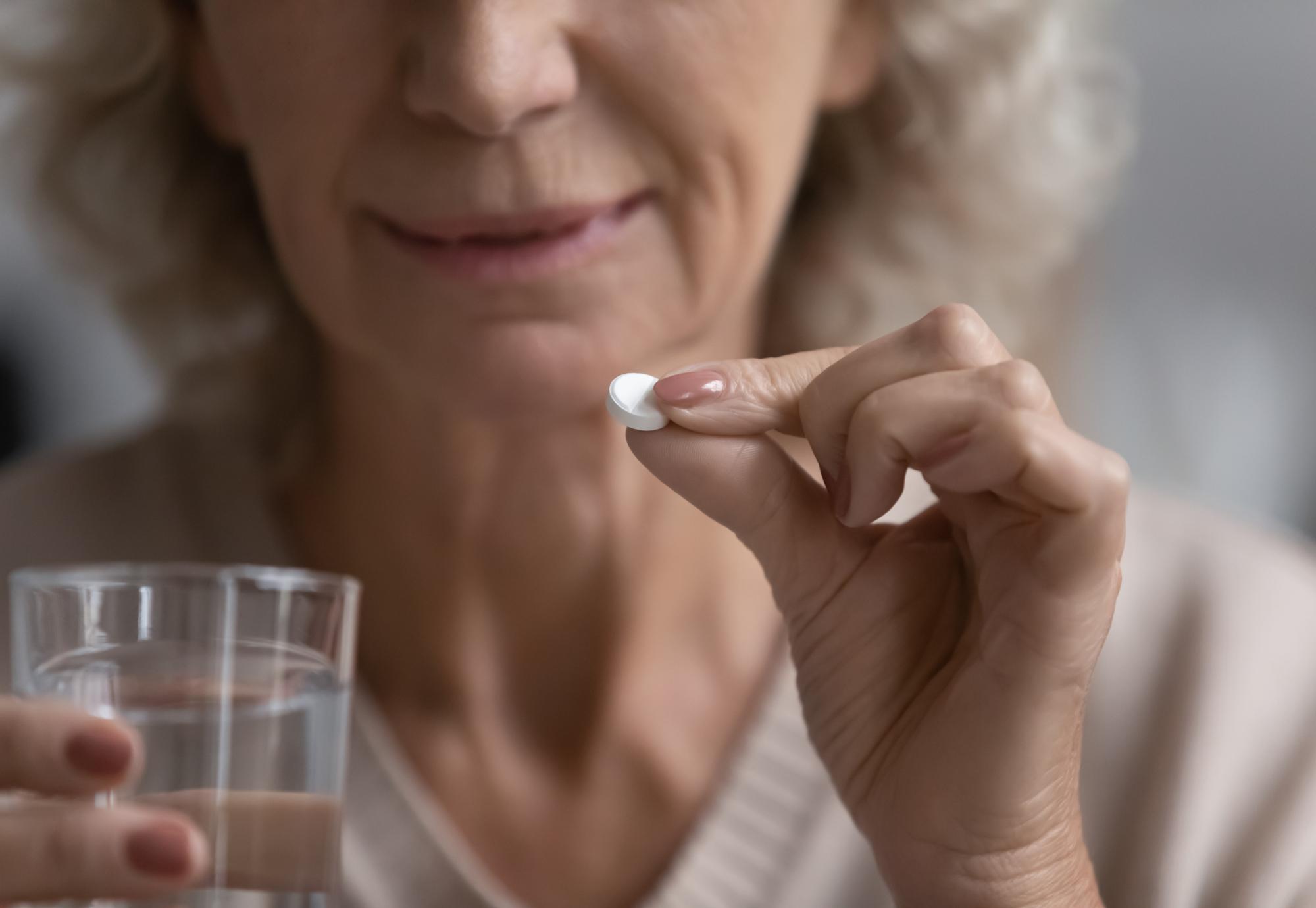 Elderly woman holds pill in her hand ready to be taken.