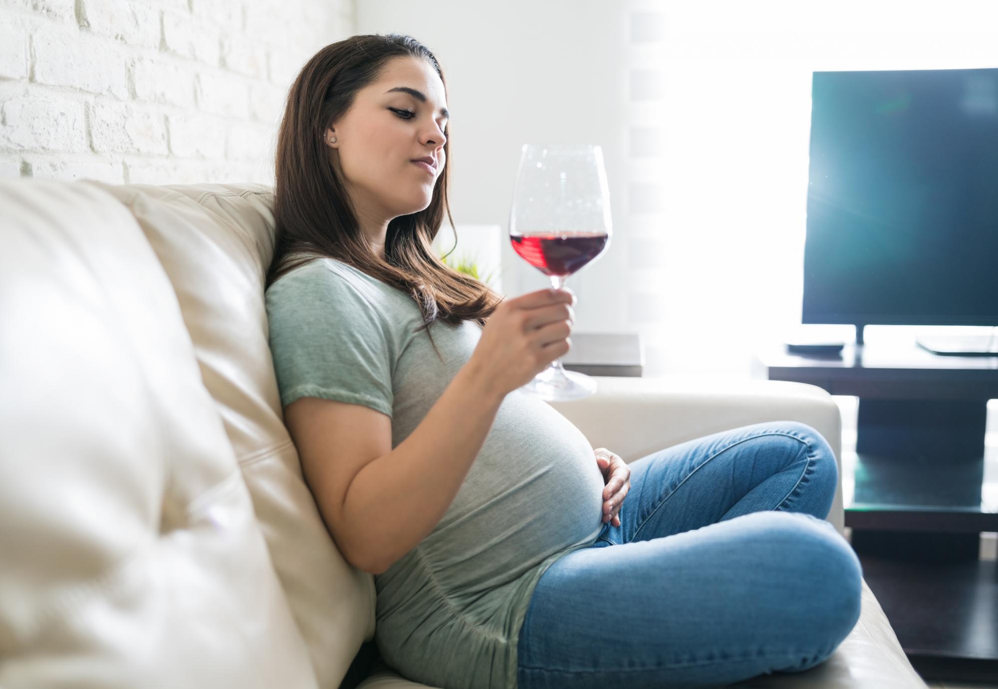 Pregnant woman enjoys glass of wine at home.