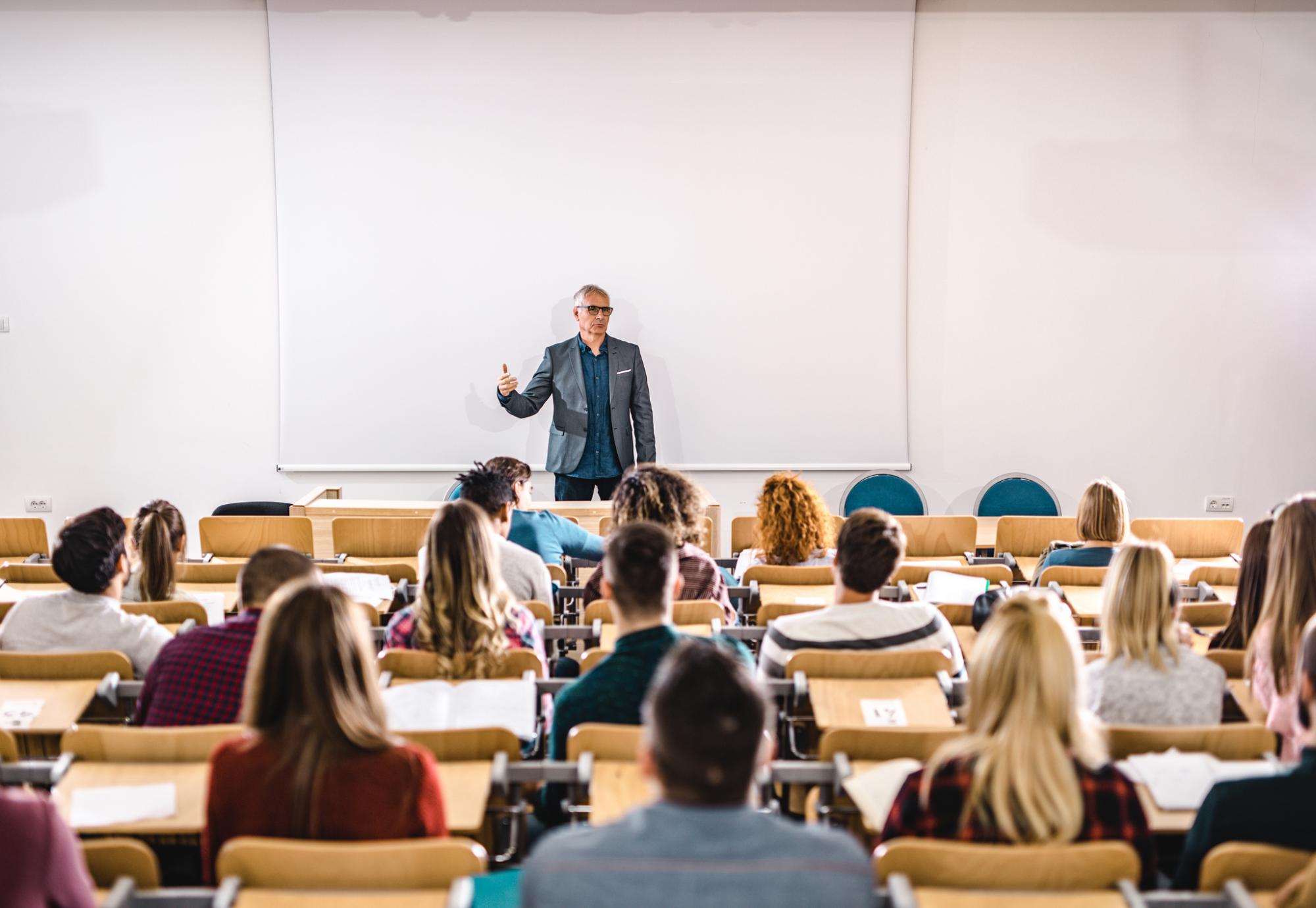 Lecturer stands teaching students in a lecture hall.