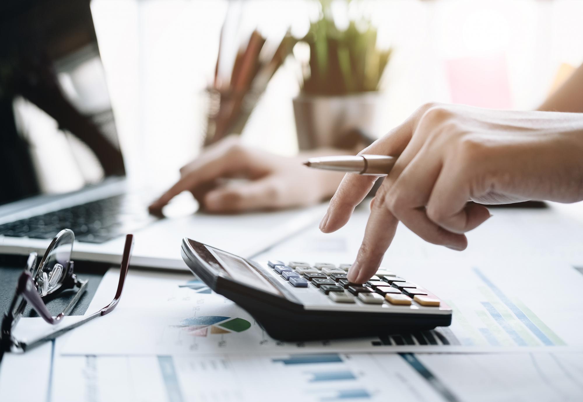 Female accountant enters numbers from calculator into computer