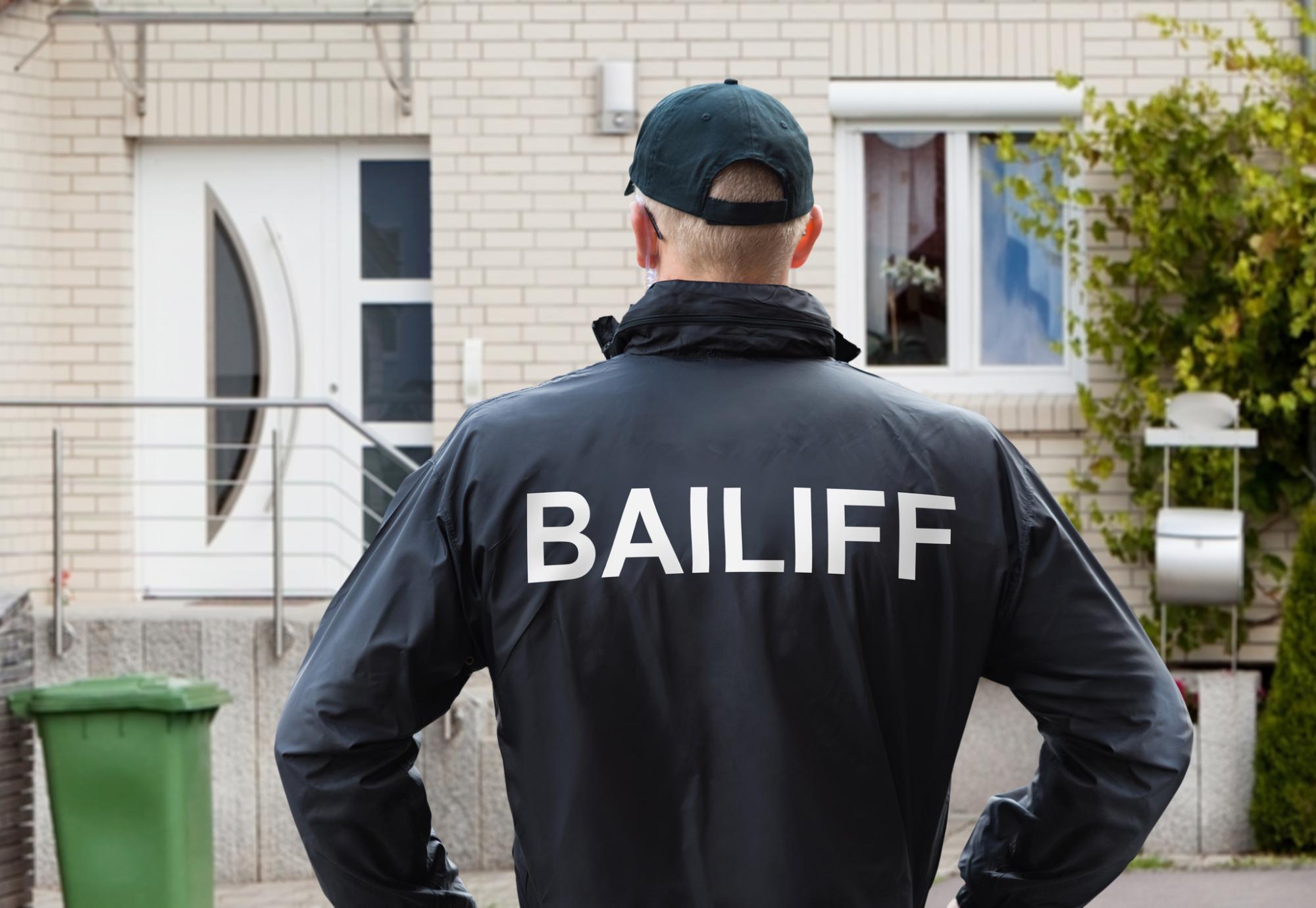 Bailiff stands in front of house ready to knock. 