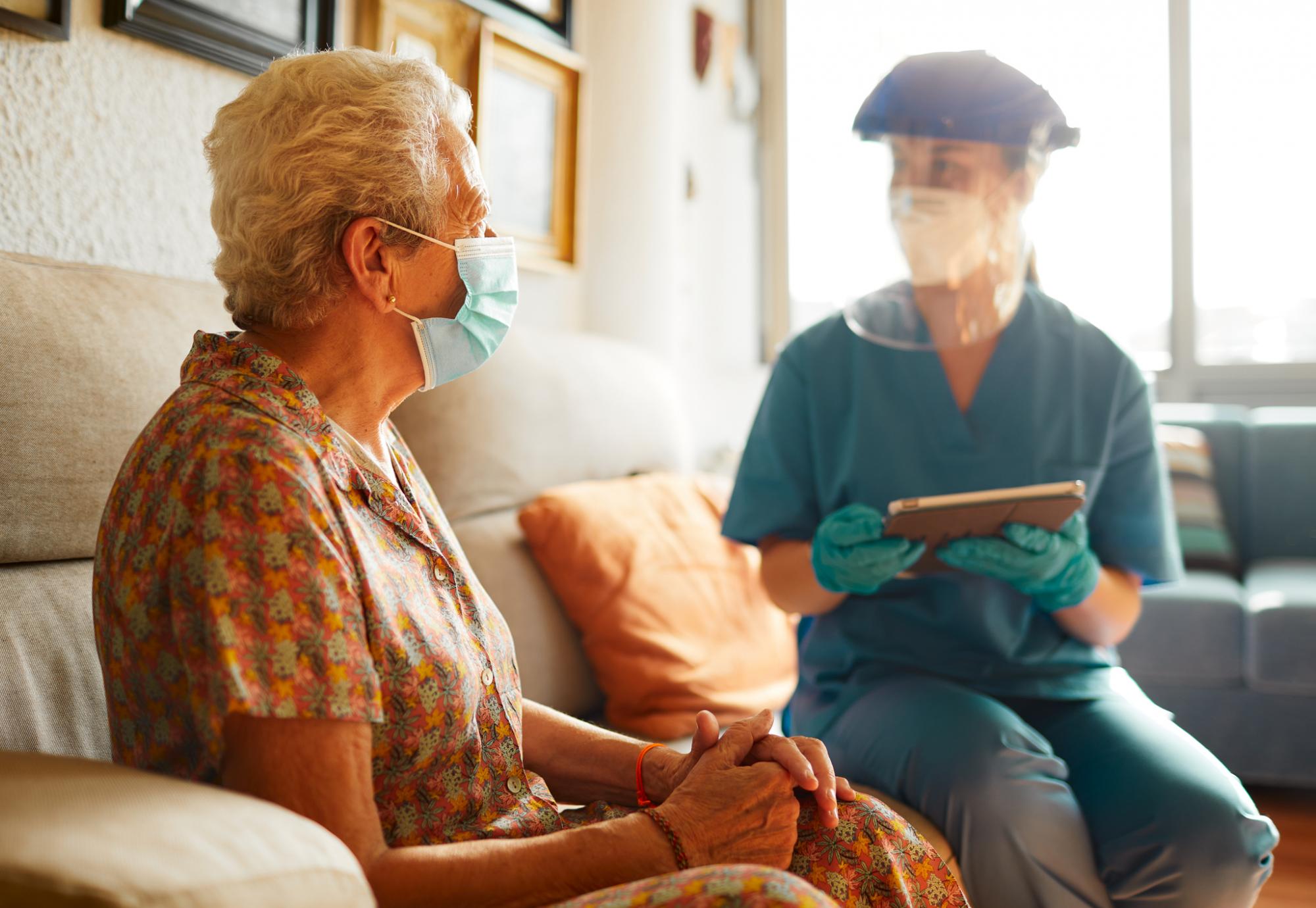 Care home nurse sits with resident in PPE. 