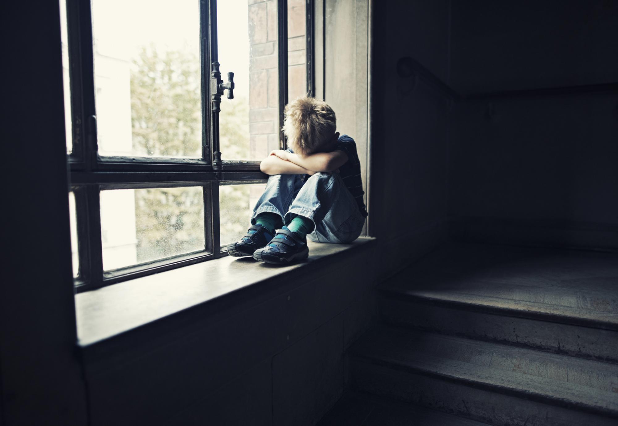 Lonely child sits in window. 