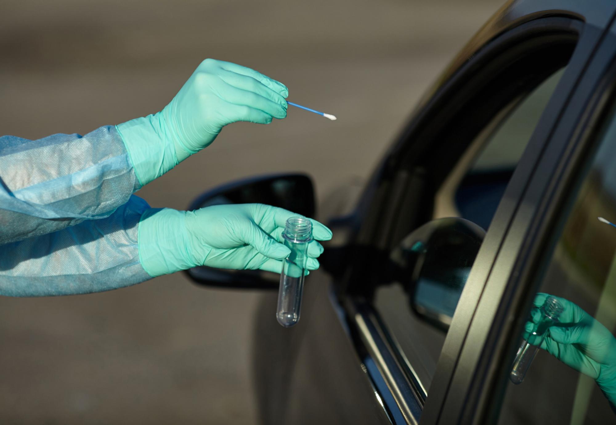 Gloved person swabs person in car for Covid.