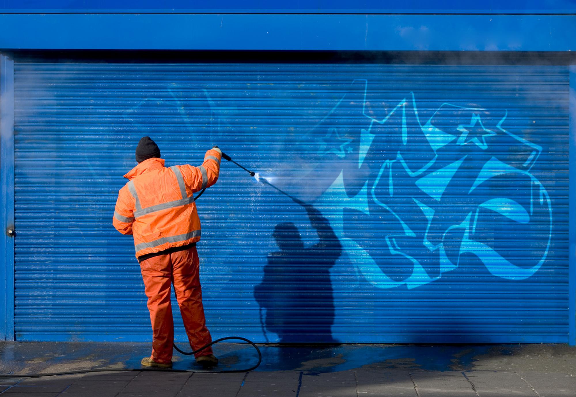 Man removes graffiti from shop front.