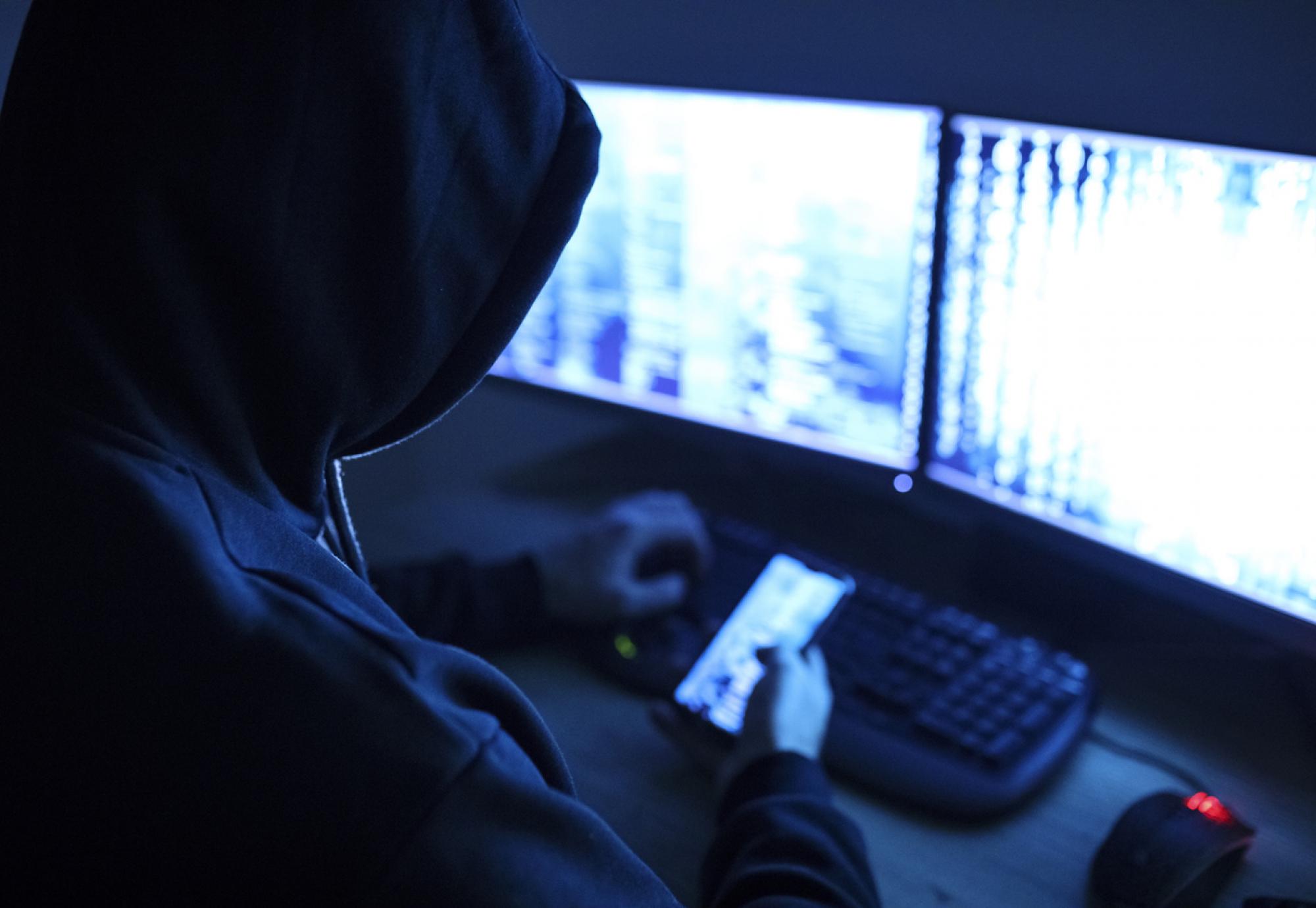 Hacker sits at computer with a digital representation of a data breach on his laptop.