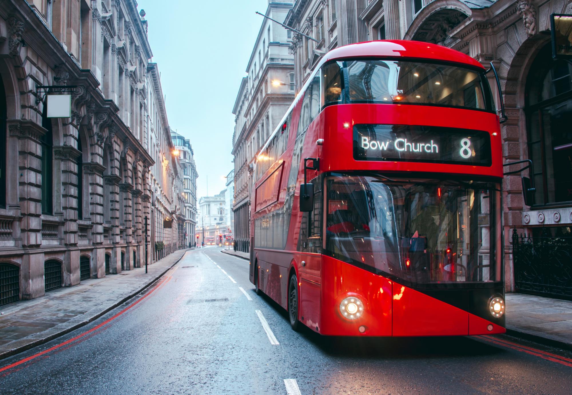 Bus drives down empty London street. 