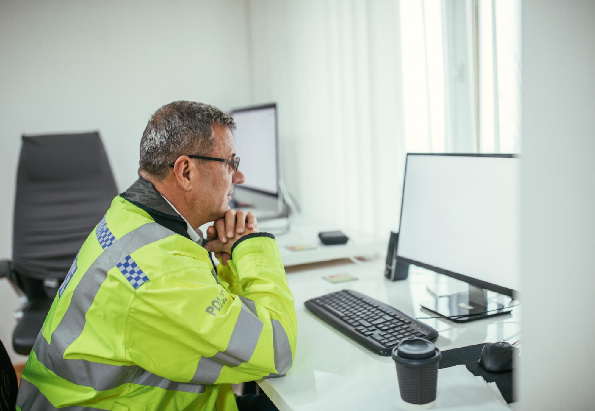 Poliec officer at a desk staring at a computer screen