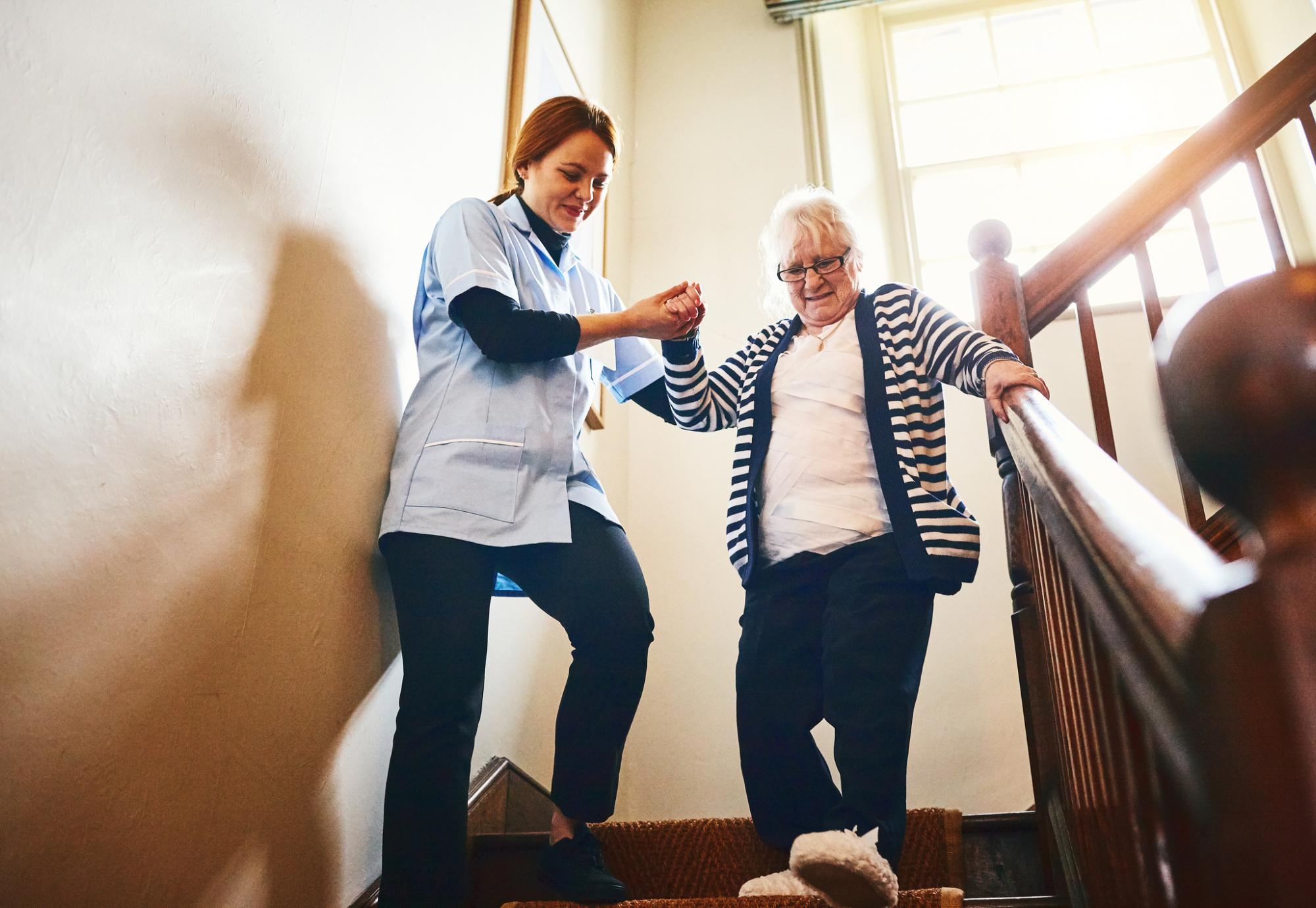 Social care worker helping woman walk down stairs