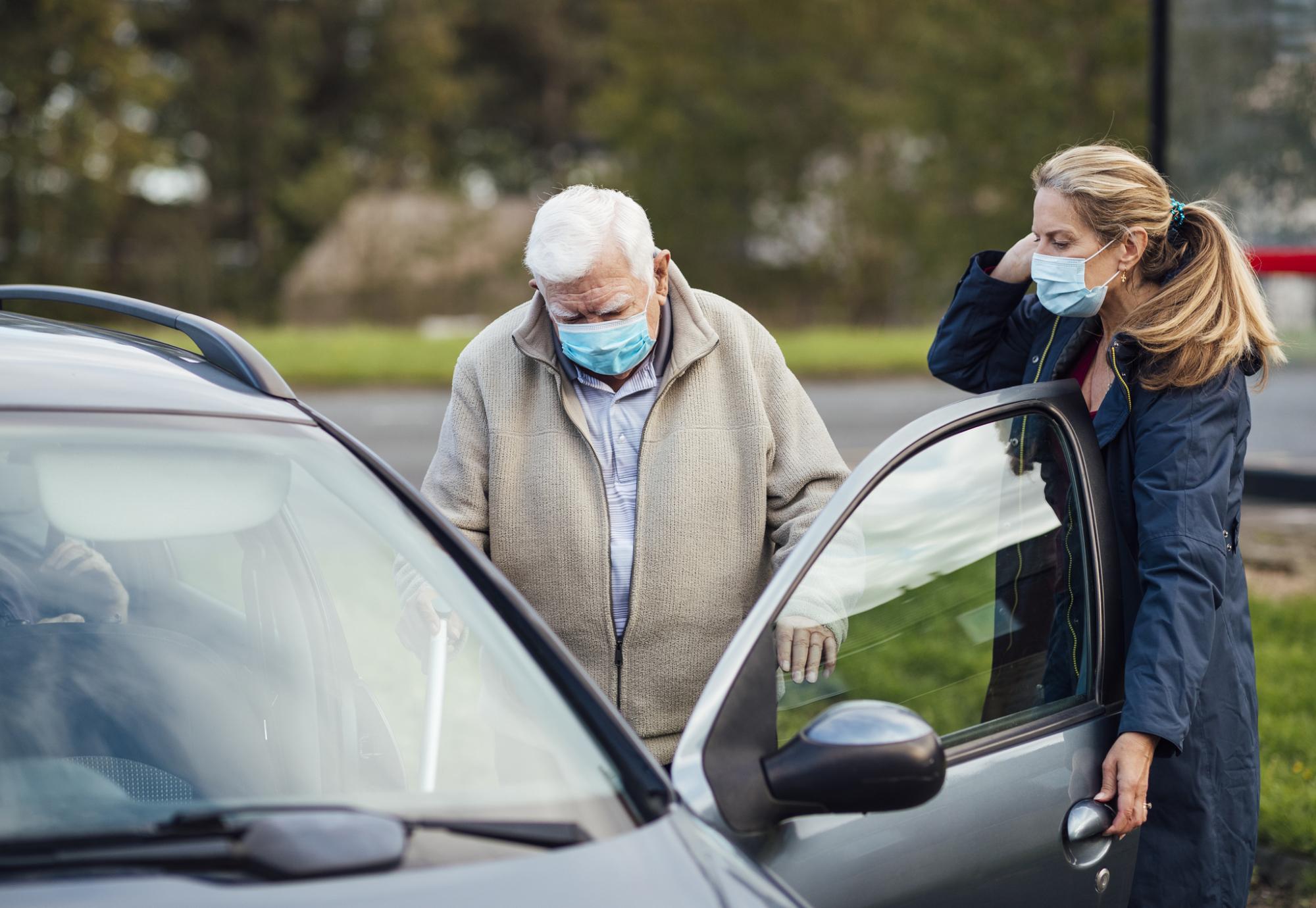 Carer helping elderly man into car