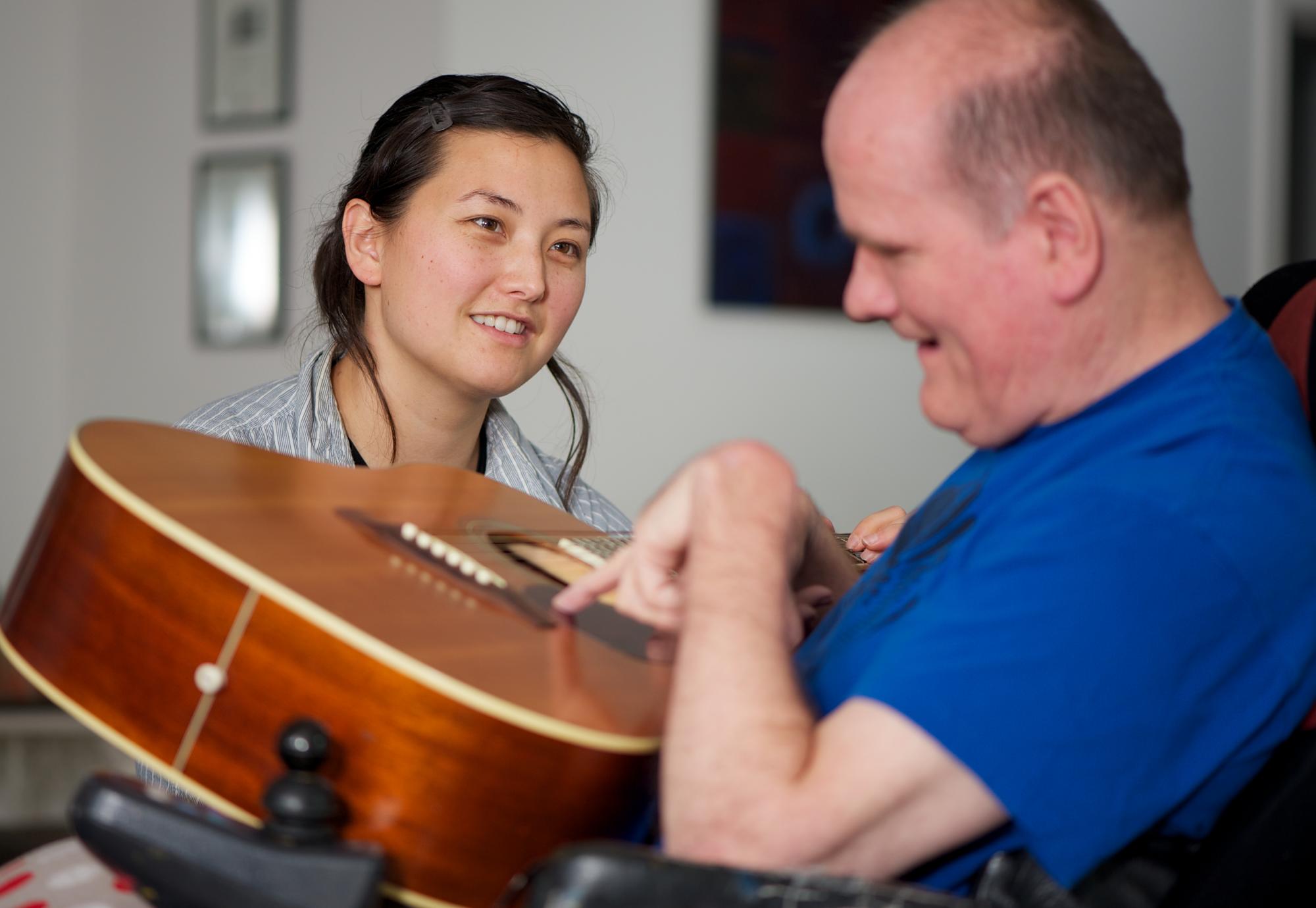 Social care worker sitting with a disabled man as he plays guitar