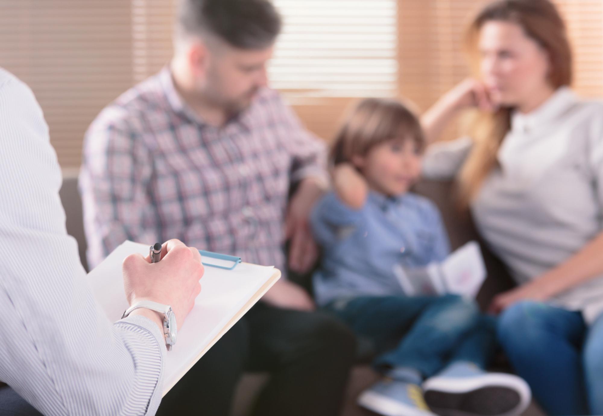 A child sits with two adults as a professional makes notes