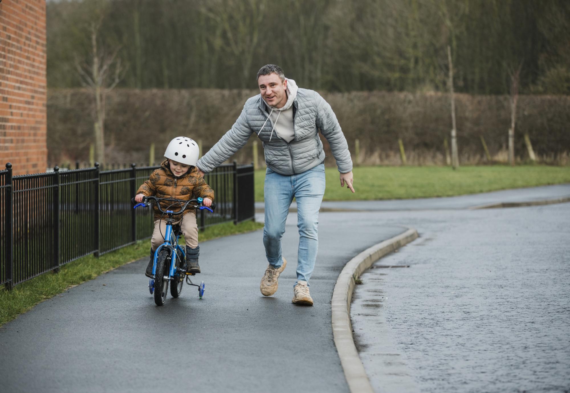 Young boy learning to ride a bike with his dad