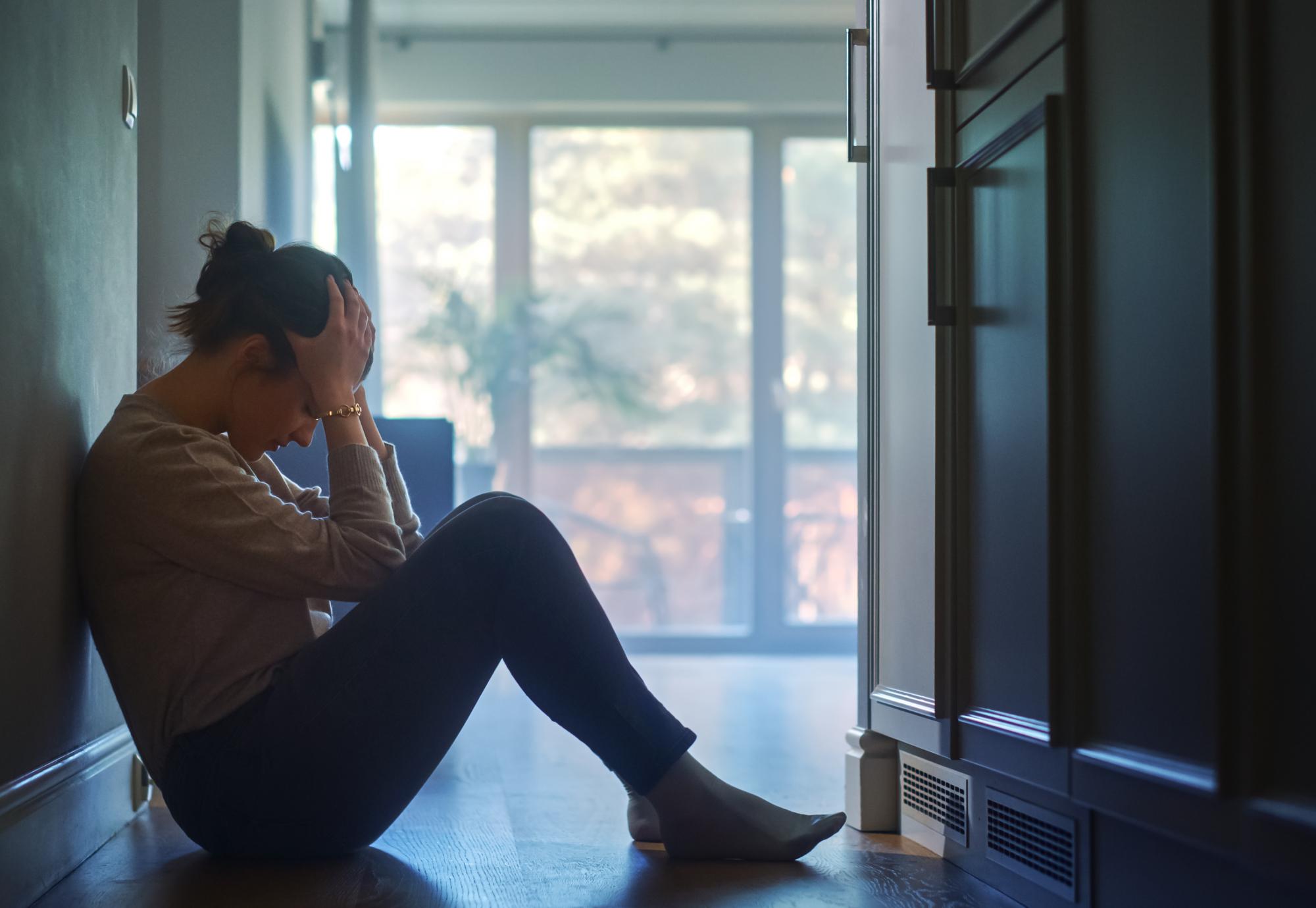 A woman sits in the hallway of her home with her head in her hands.