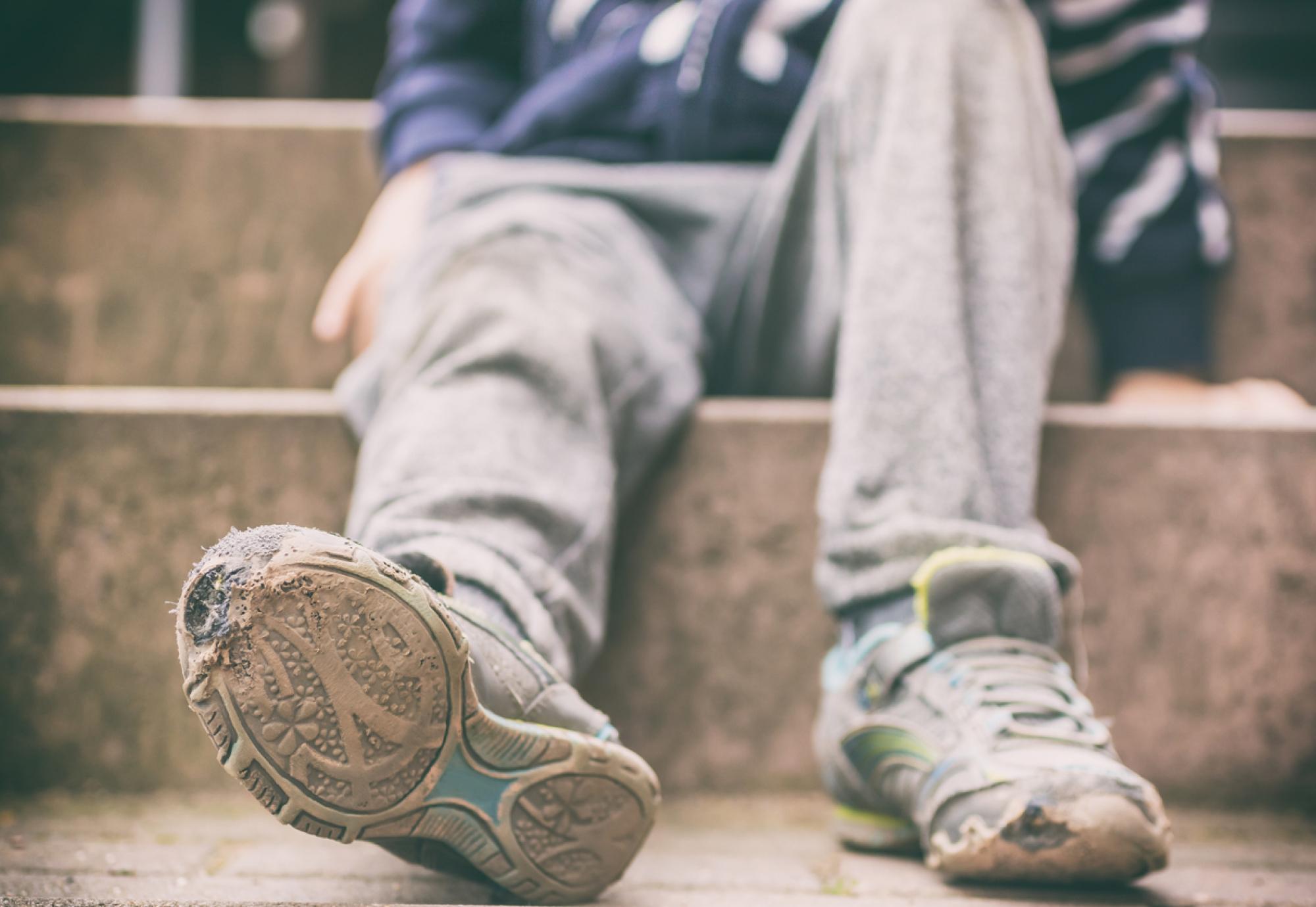 The torn shoes and dirty clothes of a child in poverty