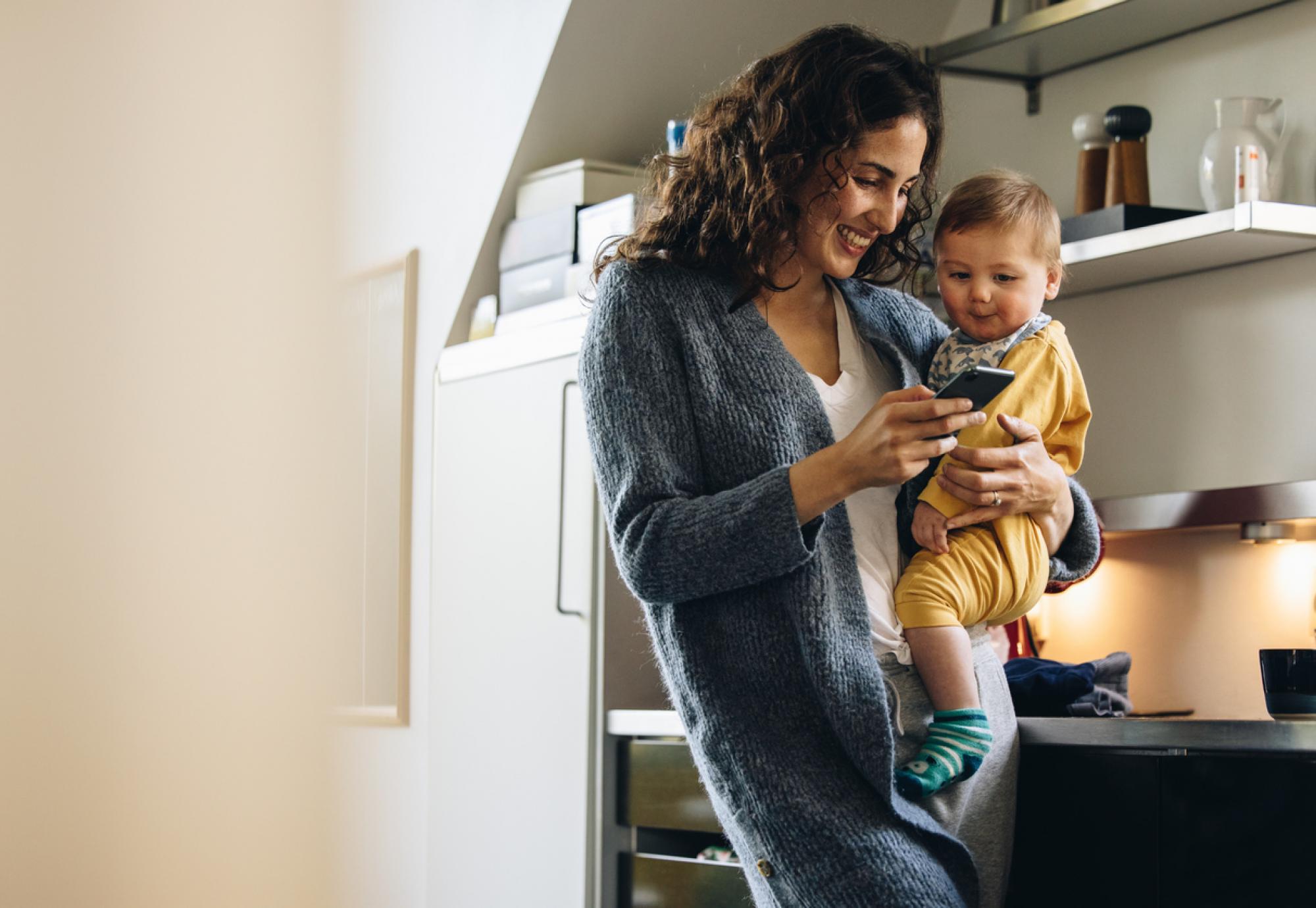 A mother holding a baby and a phone