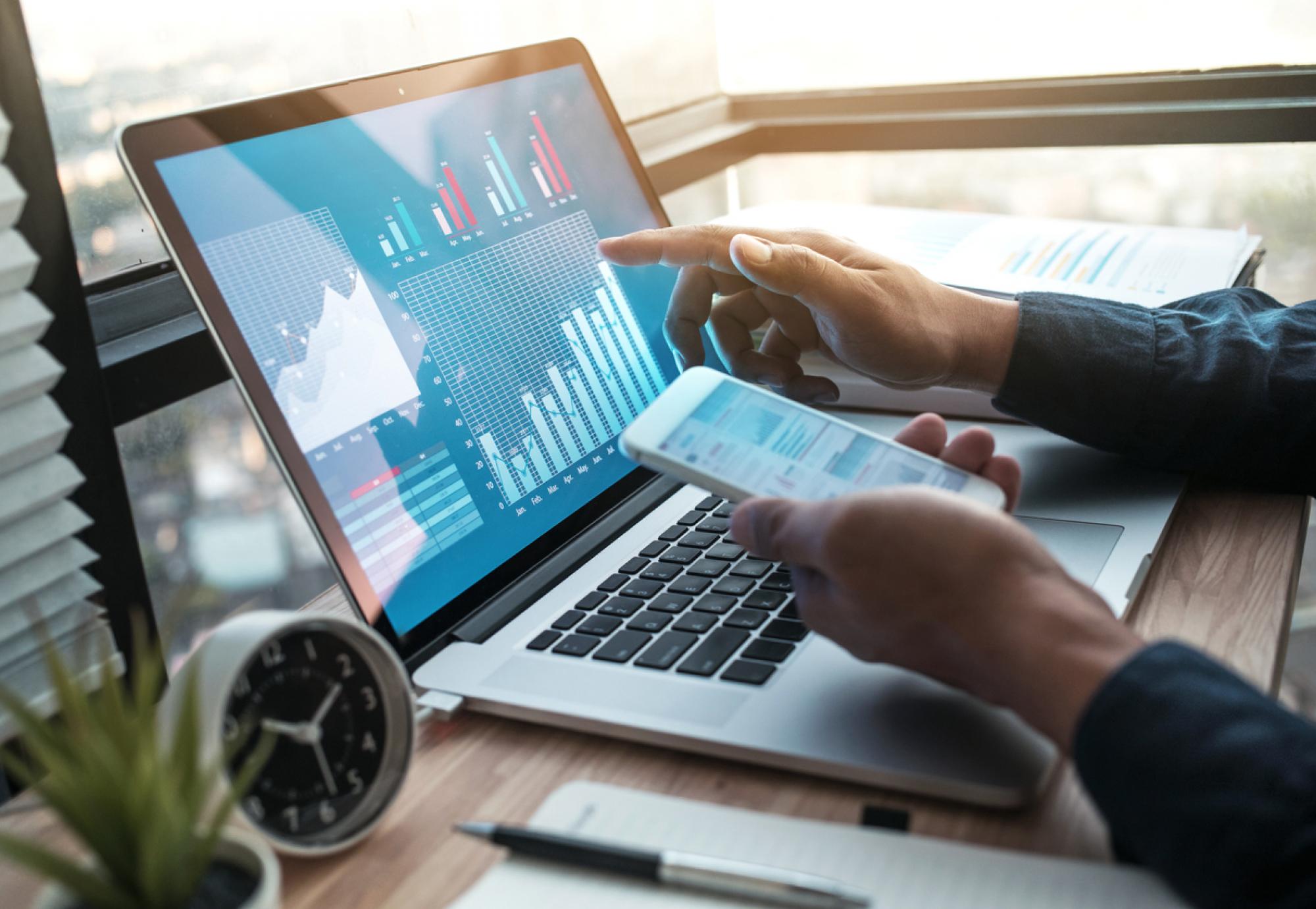 Someone doing business on a laptop and a mobile phone, with a graph on the screen