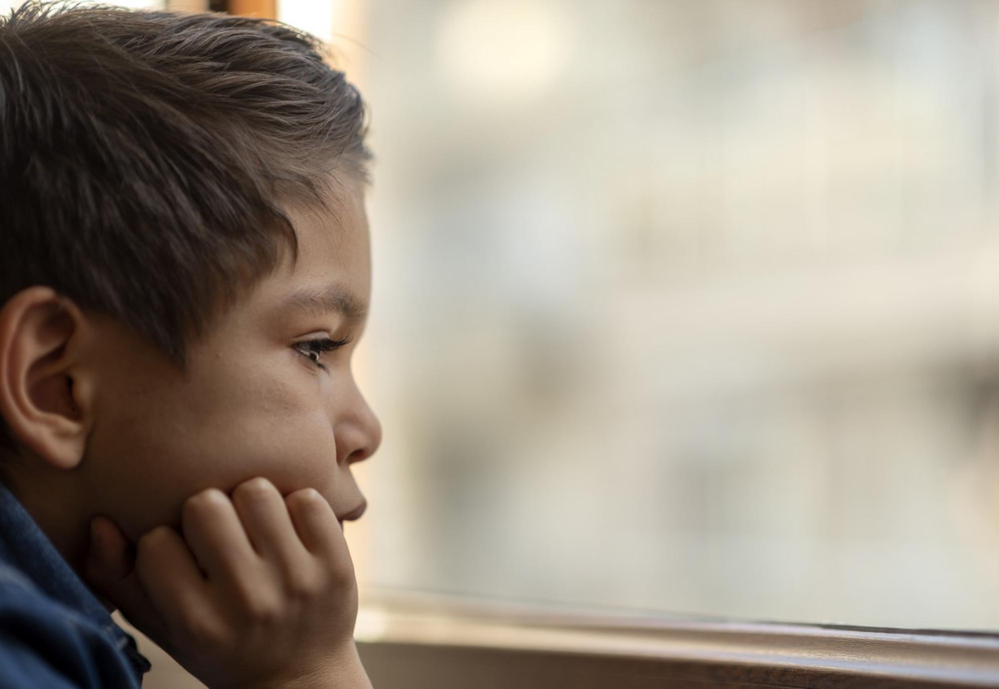 A sad child looks out of a window