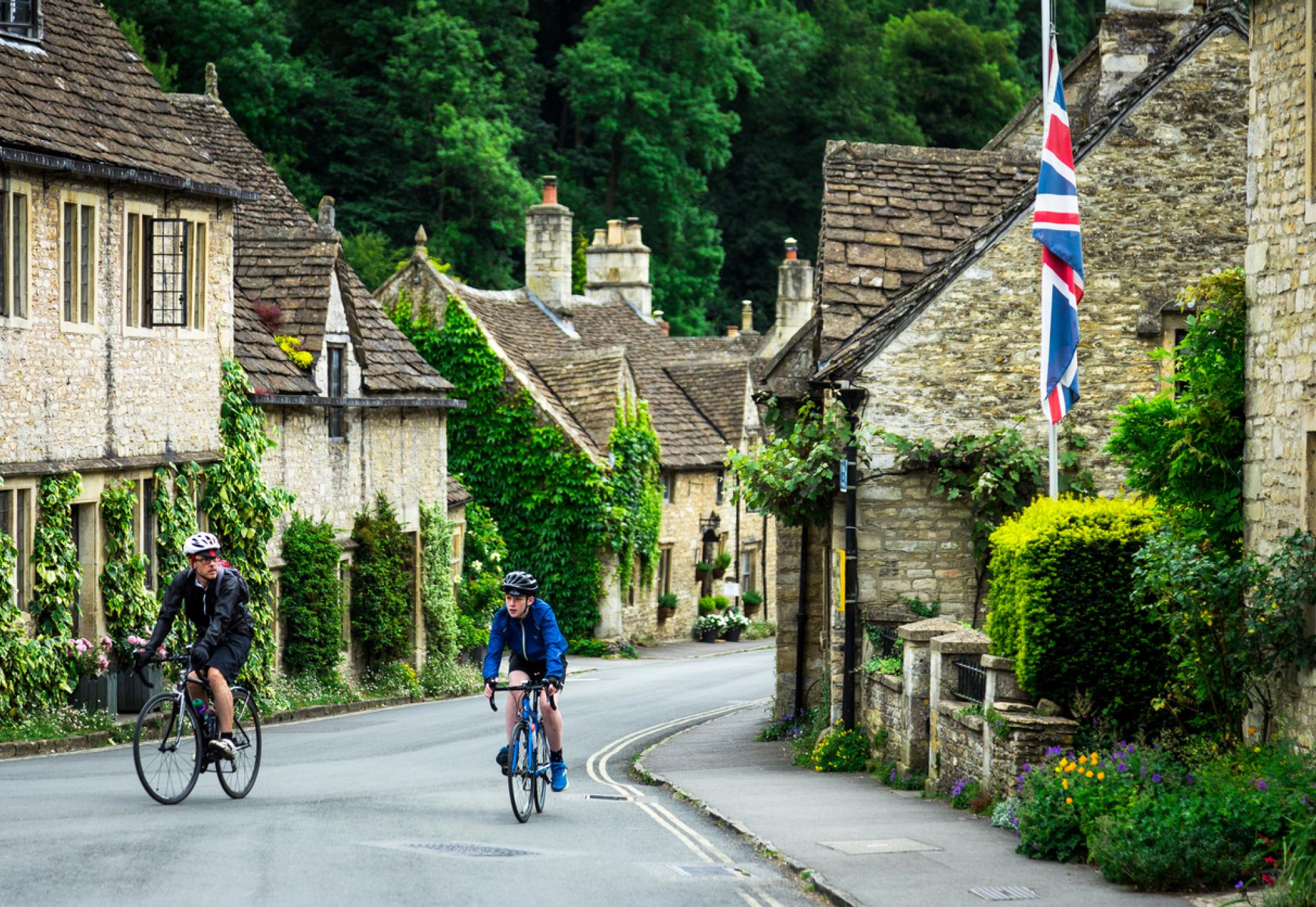 Cyclists riding bikes through a village in Cotswolds
