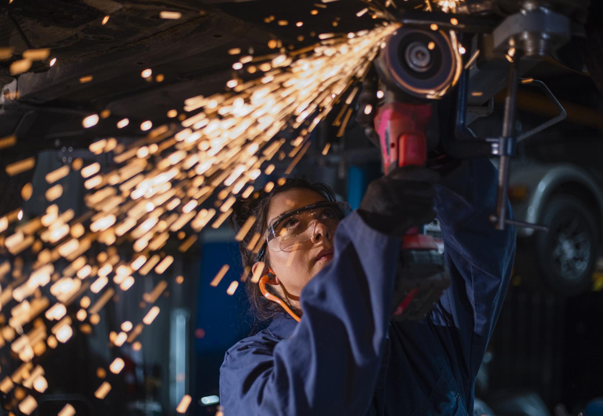 Low angle close up view of a female mechanic using an electric grinder tool on the base of a car while working at a car garage