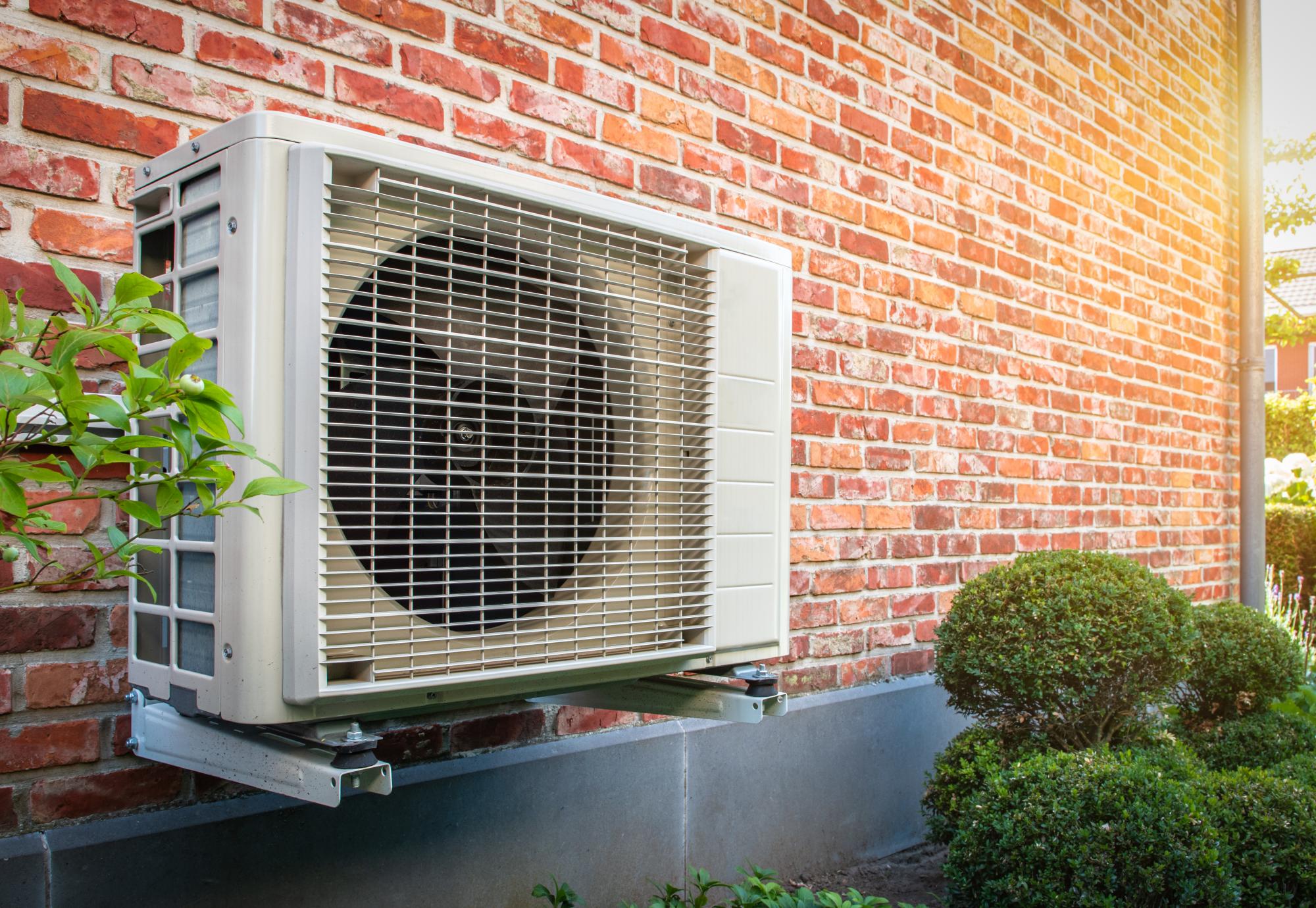 Heat pump outside a home, against a brick wall