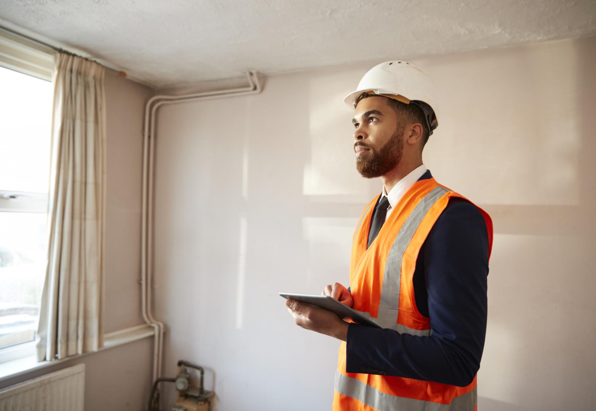 Surveyor In Hard Hat And High Visibility Jacket With Digital Tablet Carrying Out House Inspection