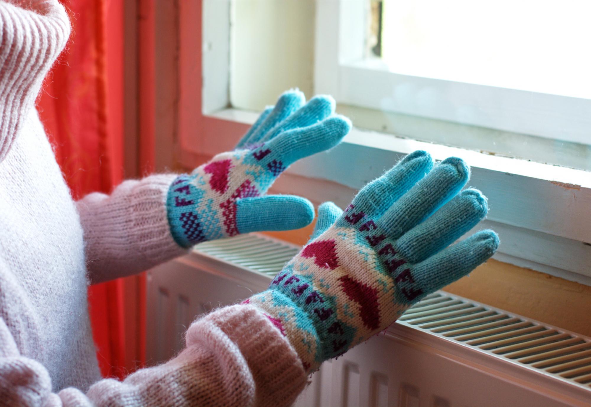 Woman heating gloved hands on raditator