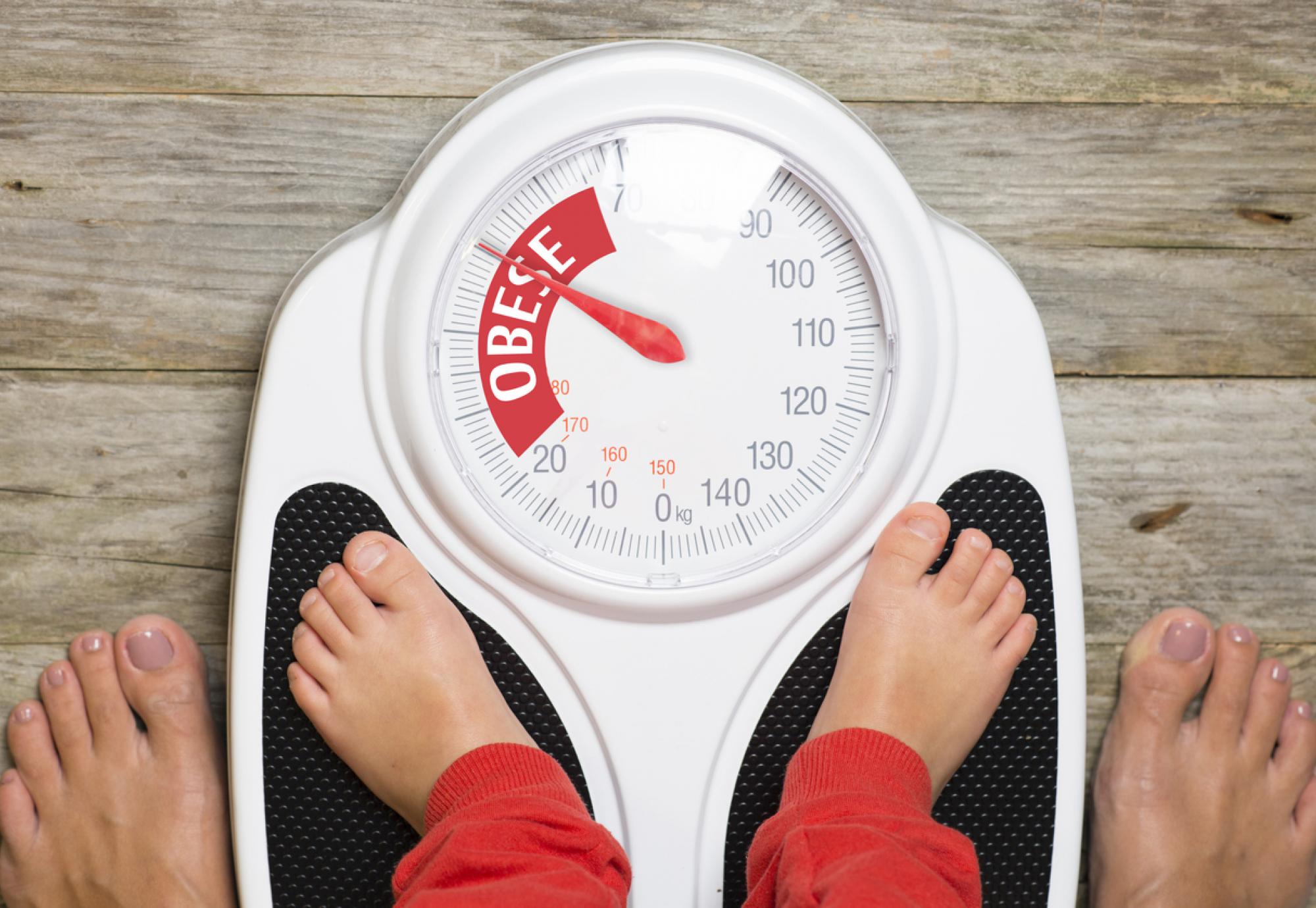 Child standing on scales pointing to 'obese'