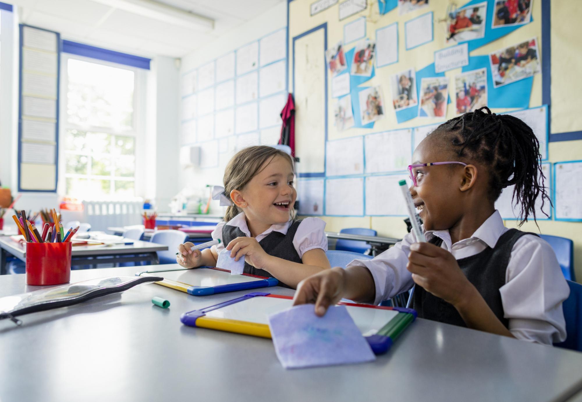 Primary school students sitting in a classroom writing on a mini whiteboards 