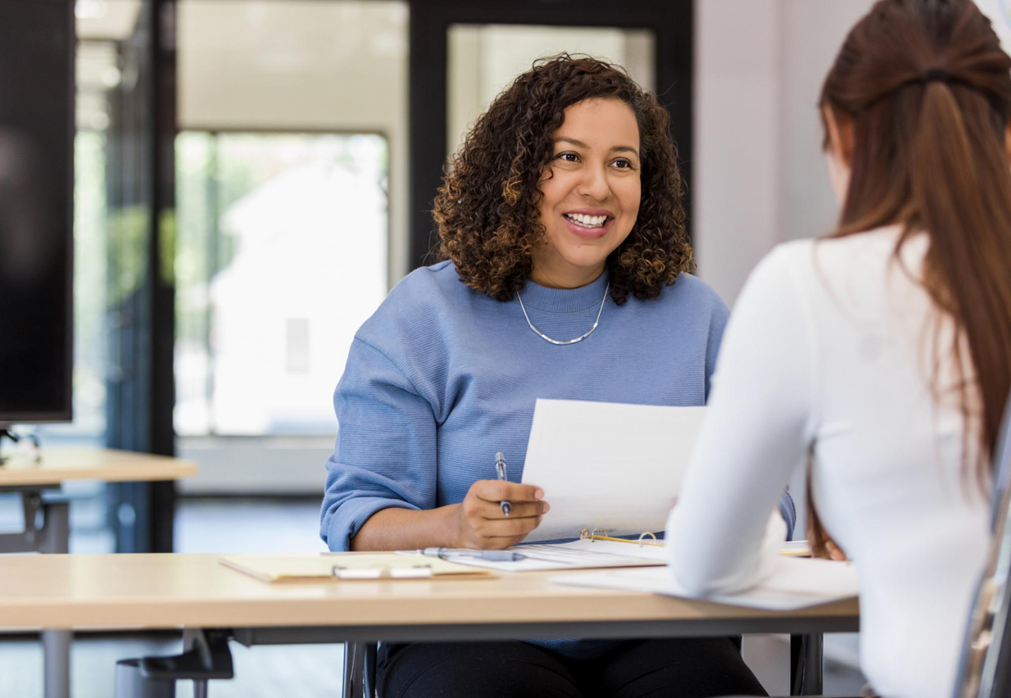 The office manager holds onto a resume while speaking with the new intern they are considering.